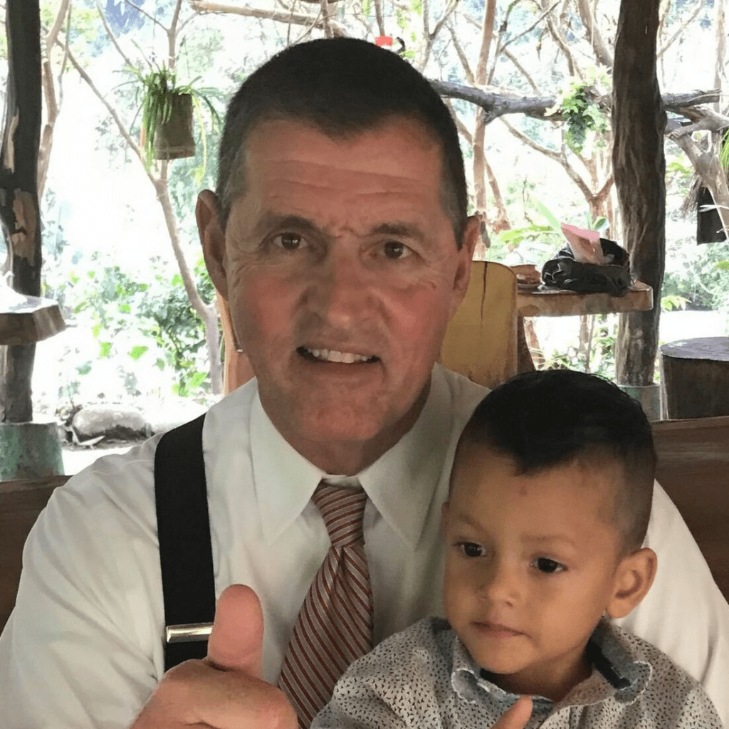 A man in a white shirt and tie gives a thumbs-up alongside a young boy in a patterned shirt