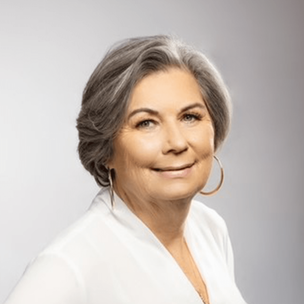 Smiling woman with gray hair and hoop earrings, wearing a white blouse