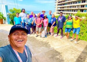 Tour group selfie with a smiling guide in foreground, surrounded by diverse participants. Captures the camaraderie during a vacation in a coastal setting.