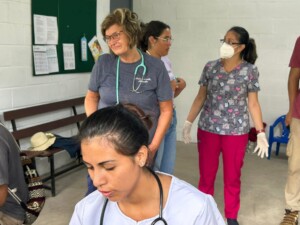 Healthcare volunteers assist in a community clinic. A nurse with a stethoscope attends to patients, while others engage in discussions.