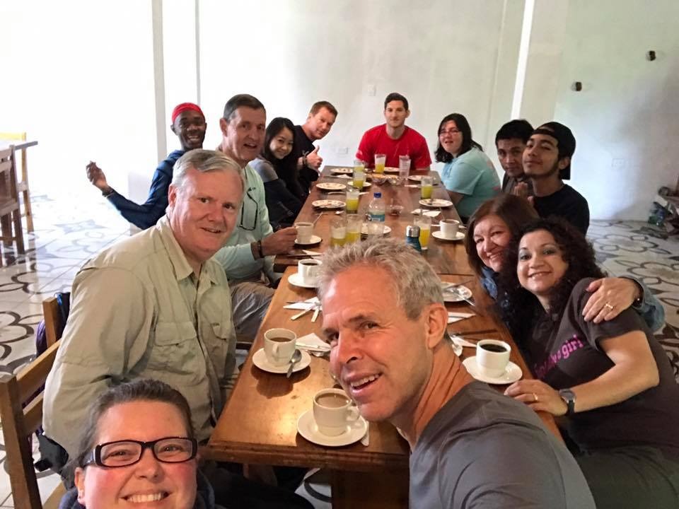 A diverse group of people enjoys breakfast around a long wooden table