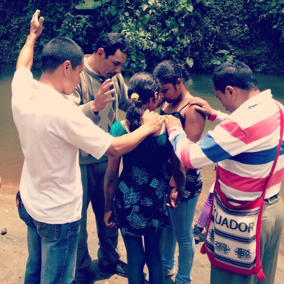 A group of individuals prays in a natural setting by a river